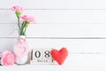 International Womens day concept. Pink carnation flower in vase and red heart with March 8 text on wooden block calendar on white Royalty Free Stock Photo