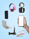 Internet shopping. Man using mobile phone with blank screen on light blue background, closeup. Different goods flying around Royalty Free Stock Photo