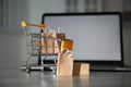 Internet shopping. Small cart with bags and box near laptop on table indoors Royalty Free Stock Photo
