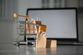 Internet shopping. Small cart with bags and box near laptop on table indoors