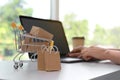 Internet shopping. Small cart with boxes and bags near woman using laptop indoors