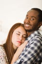 Interracial charming couple wearing casual clothes posing while embracing intimately, she has eyes closed and him