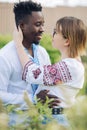 Interracial couple embraces in garden dressed in Ukrainian embroidered shirts