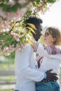 Interracial couple embraces in Ukrainian embroidered shirts near blooming sakura tree