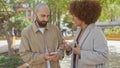 Interracial couple engaged in conversation using smartphone in a city park Royalty Free Stock Photo