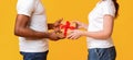 Interracial couple exchanging gifts over yellow background Royalty Free Stock Photo