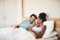 Interracial couple, laughing and relax on bed for morning bonding, funny relationship or joke at home. Happy woman and Royalty Free Stock Photo