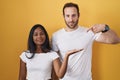 Interracial couple standing over yellow background amazed and smiling to the camera while presenting with hand and pointing with Royalty Free Stock Photo