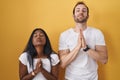 Interracial couple standing over yellow background begging and praying with hands together with hope expression on face very Royalty Free Stock Photo