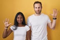 Interracial couple standing over yellow background showing and pointing up with fingers number ten while smiling confident and Royalty Free Stock Photo