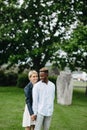 Interracial couple stands, holds hands and kisses in park on background of statue Polovtsian woman Royalty Free Stock Photo