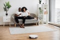 Interracial couple using laptop while robot cleaning floor