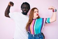 Interracial couple wearing casual clothes showing arms muscles smiling proud