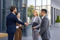 Interracial group of young business people standing on street outside office building in suits, man and woman shaking Royalty Free Stock Photo