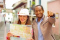 Interracial happy couple wearing casual clothes in urban envrionment, interacting and looking at map