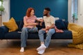 Unhappy young diverse married couple sitting on sofa talking about problems in relationship Royalty Free Stock Photo