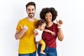 Interracial young family of black mother and hispanic father with daughter pointing to the back behind with hand and thumbs up, Royalty Free Stock Photo