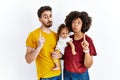 Interracial young family of black mother and hispanic father with daughter pointing up looking sad and upset, indicating direction Royalty Free Stock Photo