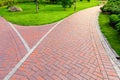 the intersection of footpaths of red tiles and a drainage grid in a park.