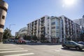 An intersection at Grand Ave and Olympic Blvd with a white and brown apartment building, cars driving and people walking