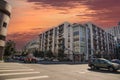 An intersection at Grand Ave and Olympic Blvd with a white and brown apartment building, cars driving and people walking