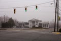 An intersection looking at green lights and a funeral home on a cold foggy morning