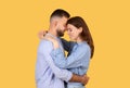 Intimate couple embracing and touching foreheads lovingly on yellow background