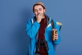 Intrepid young explorer closing his eyes, covering his mouth with hand, yawning, having binoculars around neck, holding mug with Royalty Free Stock Photo