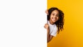 Black girl peeking out blank white advertising billboard at studio