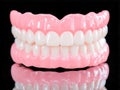 A set of realistic full upper and lower dentures displayed against a black background with a reflective surface highlighting the Royalty Free Stock Photo