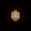 Intricately designed, hanging lantern with a warm glow against a dark background. The Royalty Free Stock Photo