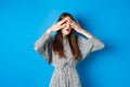 Intrigued young girl peeking through fingers with excitement, seeing interesting thing, standing on blue background Royalty Free Stock Photo