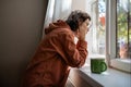 Introverted teen girl standing near window, looking at street indifferently, thinking of life