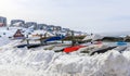 Inuit kayaks stored for a winter time in snow with Modern buildings and small cottages in the background, Nuuk old city harbor,