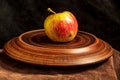 An inverted clay plate is located on a leather stand. On the plate is a red apple. Black background. Royalty Free Stock Photo