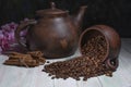 An inverted mug with coffee beans on the background of a clay teapot, sugar cubes,cinnamon sticks and cherry blossoms on a wooden Royalty Free Stock Photo