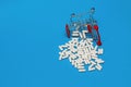 Inverted trolley with purchased medicines, scattered pills on a blue background, medical concept