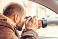 Investigator or private detective or reporter or paparazzi sitting in car and taking photo with professional camera Royalty Free Stock Photo