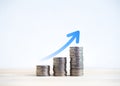 Rising up big blue arrow on coin stack as a growth graph chart step on wood table and white background. Royalty Free Stock Photo