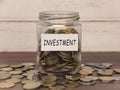 Investment label on coin jar on top of wooden desk with asorted coins background.