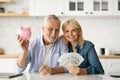 Investments Concept. Smiling Senior Couple Holding Piggybank And Dollar Cash At Home Royalty Free Stock Photo