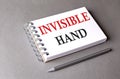 INVISIBLE HAND word on notebook on grey background