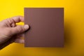 Invitation Mock-Up, square Flyer in male hands, holding a brown paper blank on a yellow background