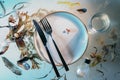 Invitation to a seafood dinner, plate with cutlery, water and salt shaker among seaweed, shells and sand arranged like swimming on