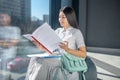 Involved young brunette female sitting on bag chair, looking through papers, smiling