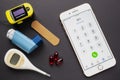 An iPhone with the 911 dial emergency services, with an asthma inhaler, a bandage, some pills, and an oximeter on a black