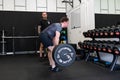 Ipswich Suffolk UK April 03 2022: Muscular young man working out with a barbell in a small gym being coached by a personal trainer