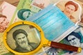 Iranian currency, anti-virus mask and magnifying glass. The concept of the country`s economy during the coronavirus pandemic