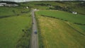 Ireland rural road aerial shot: cars riding near crossway. Cottages, meadows, fields on hills