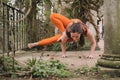 Irish female new yoga teacher doing a dragonfly pose wearing orange sportswear in the terrace of a historic landscaped garden in